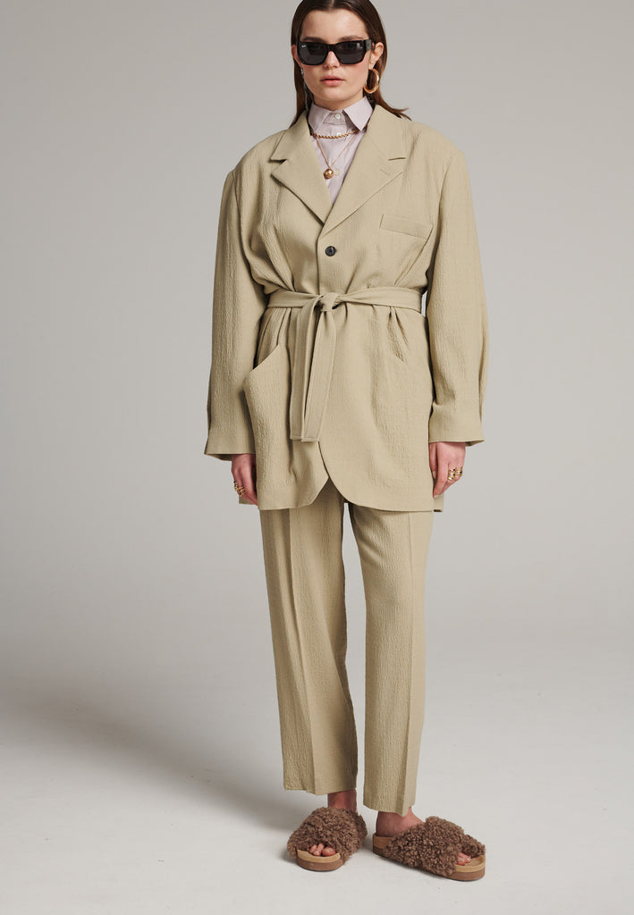 Seasonless oversized tailored blazer in stone with a round-shouldered silhouette and coordinating belt that creates some gathering at the back to temper the fitting. Play with it and tie at the smallest part of your waist or tie it at the back for a sense of ease.
