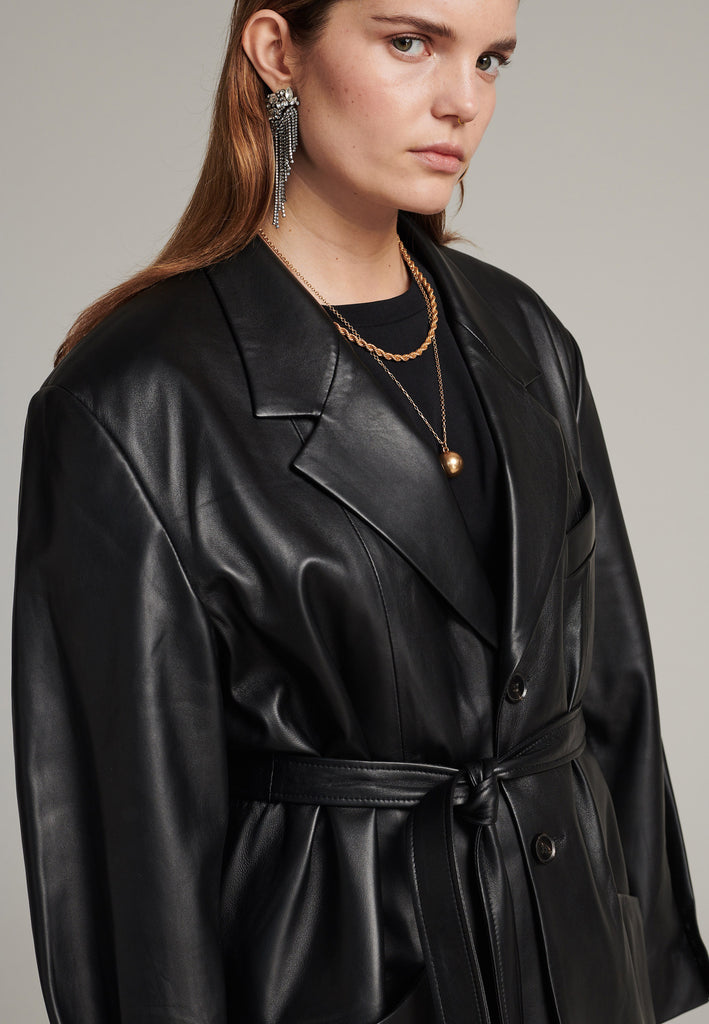 Seasonless oversized leather blazer in black with round-shouldered silhouette and coordinating belt that creates some gathering at the back to temper the fitting. Play with it and tie at the smallest part of your waist or tie it at the back for a sense of ease. Pockets, horn buttons and fully lined with. Double fun: wear it as a blazer or as a jacket.