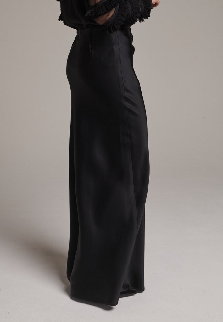 Flowy black skirt with a refined, elongated silhouette. Crafted from lightweight fabric with soft movement and an elegant drape. Front and back darts are intentionally exposed, adding subtle structure and a tailored finish to the fluid shape. A quiet statement piece, effortlessly balancing form and flow.