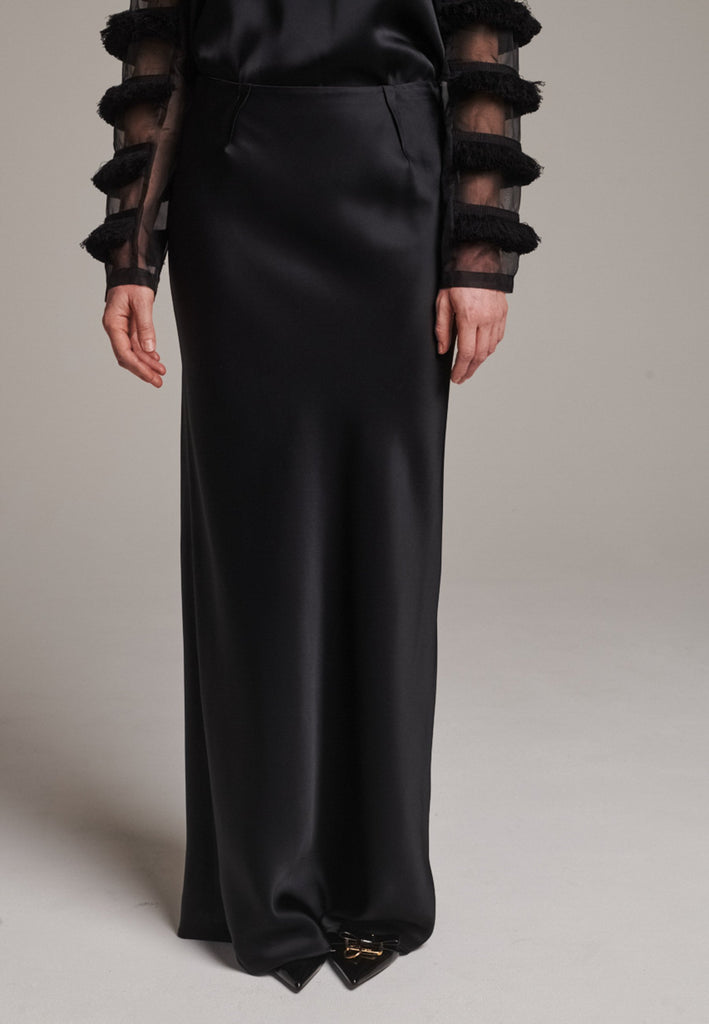 Flowy black skirt with a refined, elongated silhouette. Crafted from lightweight fabric with soft movement and an elegant drape. Front and back darts are intentionally exposed, adding subtle structure and a tailored finish to the fluid shape. A quiet statement piece, effortlessly balancing form and flow.