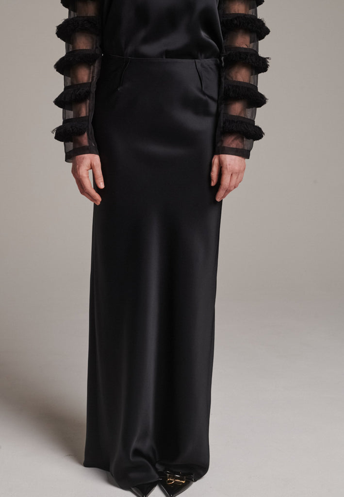 Flowy black skirt with a refined, elongated silhouette. Crafted from lightweight fabric with soft movement and an elegant drape. Front and back darts are intentionally exposed, adding subtle structure and a tailored finish to the fluid shape. A quiet statement piece, effortlessly balancing form and flow.