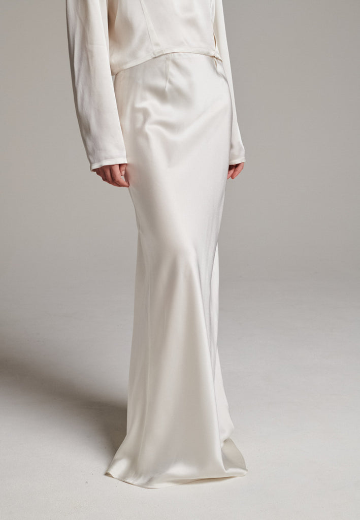 Flowy ivory skirt with a refined, elongated silhouette. Crafted from lightweight fabric with soft movement and an elegant drape. Front and back darts are intentionally exposed, adding subtle structure and a tailored finish to the fluid shape. A quiet statement piece, effortlessly balancing form and flow.