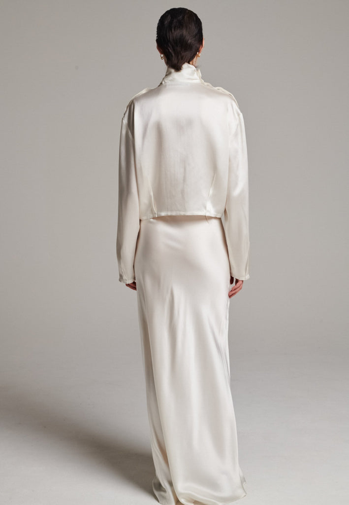 Flowy ivory skirt with a refined, elongated silhouette. Crafted from lightweight fabric with soft movement and an elegant drape. Front and back darts are intentionally exposed, adding subtle structure and a tailored finish to the fluid shape. A quiet statement piece, effortlessly balancing form and flow.