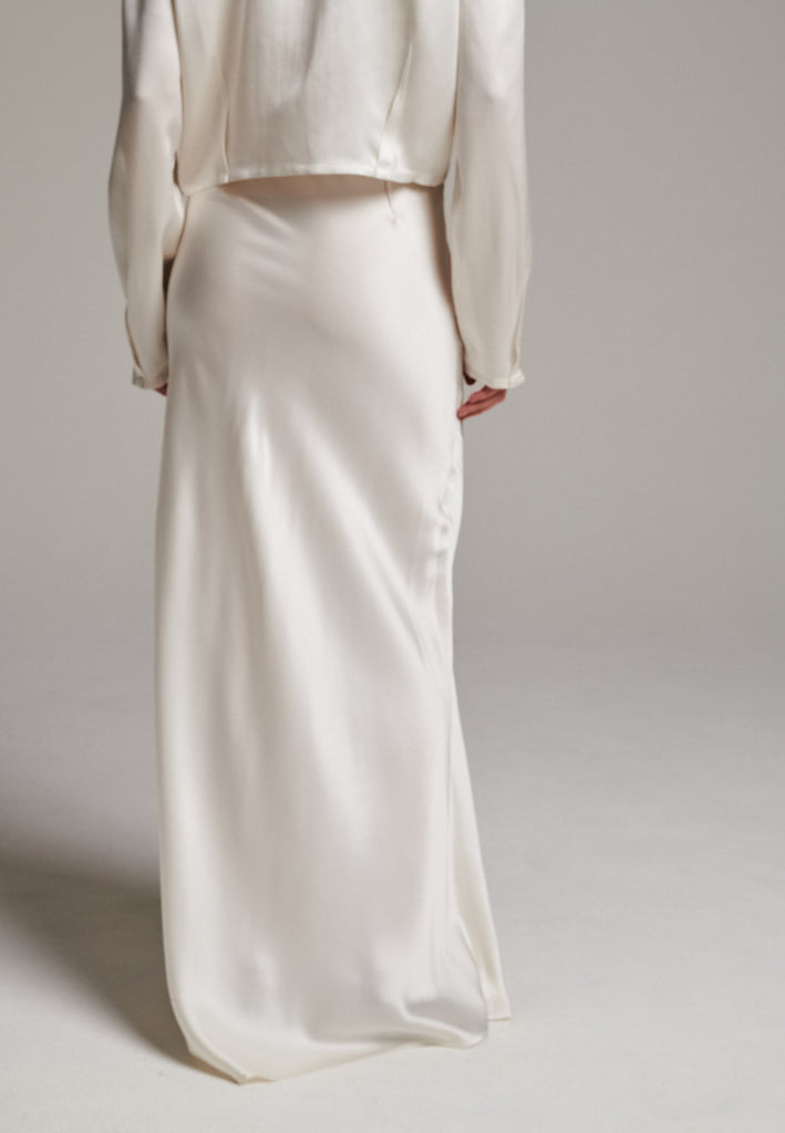 Flowy ivory skirt with a refined, elongated silhouette. Crafted from lightweight fabric with soft movement and an elegant drape. Front and back darts are intentionally exposed, adding subtle structure and a tailored finish to the fluid shape. A quiet statement piece, effortlessly balancing form and flow.