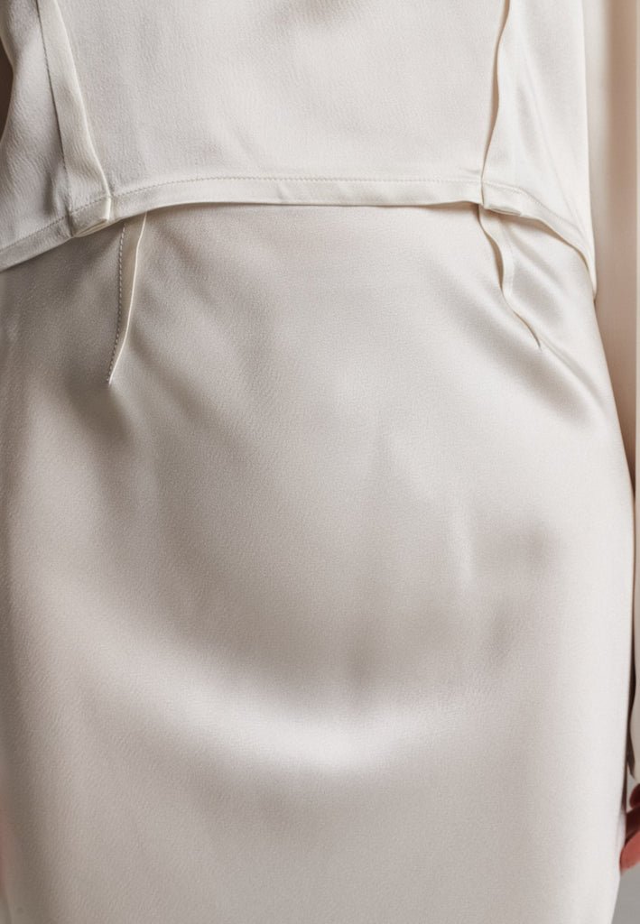 Flowy ivory skirt with a refined, elongated silhouette. Crafted from lightweight fabric with soft movement and an elegant drape. Front and back darts are intentionally exposed, adding subtle structure and a tailored finish to the fluid shape. A quiet statement piece, effortlessly balancing form and flow.