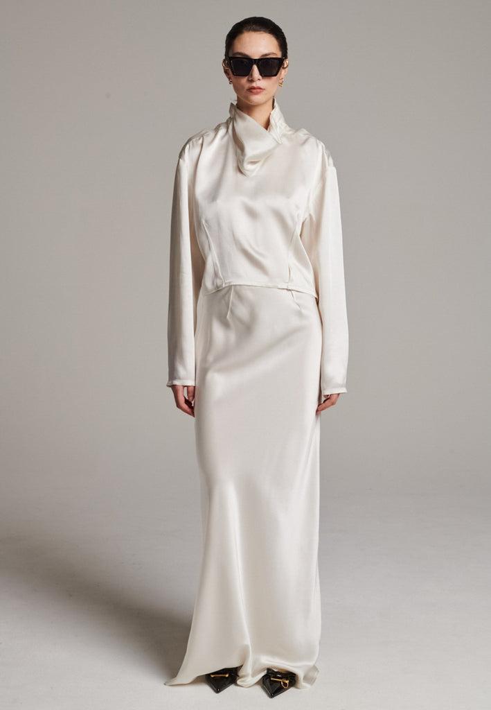 Flowy ivory skirt with a refined, elongated silhouette. Crafted from lightweight fabric with soft movement and an elegant drape. Front and back darts are intentionally exposed, adding subtle structure and a tailored finish to the fluid shape. A quiet statement piece, effortlessly balancing form and flow.