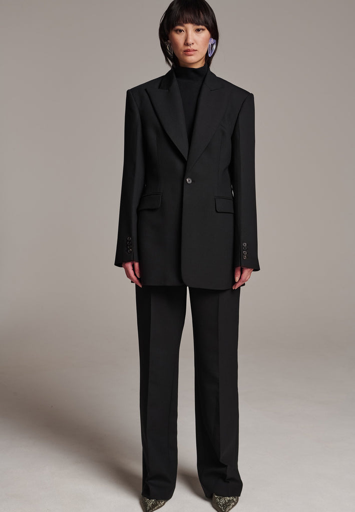 Experience flawless tailoring with this structured blazer, featuring sharp wide shoulders and a subtly cinched waist. Fully satin-lined for added luxury, it includes horn buttons and welt pockets with flaps, along with a back slit for ease of movement. Masterfully crafted in a versatile black hue, this blazer seamlessly complements a range of colors, embodying precision and elegance.