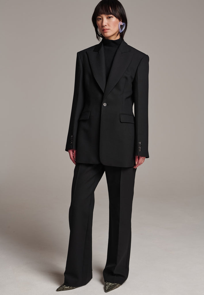 Experience flawless tailoring with this structured blazer, featuring sharp wide shoulders and a subtly cinched waist. Fully satin-lined for added luxury, it includes horn buttons and welt pockets with flaps, along with a back slit for ease of movement. Masterfully crafted in a versatile black hue, this blazer seamlessly complements a range of colors, embodying precision and elegance.