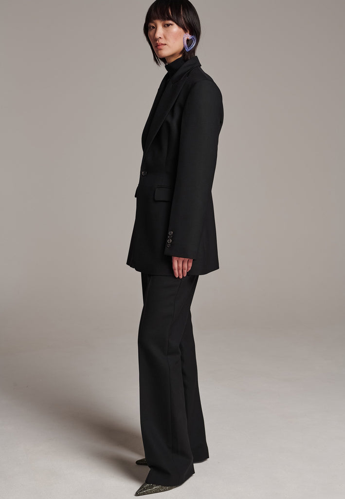 Experience flawless tailoring with this structured blazer, featuring sharp wide shoulders and a subtly cinched waist. Fully satin-lined for added luxury, it includes horn buttons and welt pockets with flaps, along with a back slit for ease of movement. Masterfully crafted in a versatile black hue, this blazer seamlessly complements a range of colors, embodying precision and elegance.