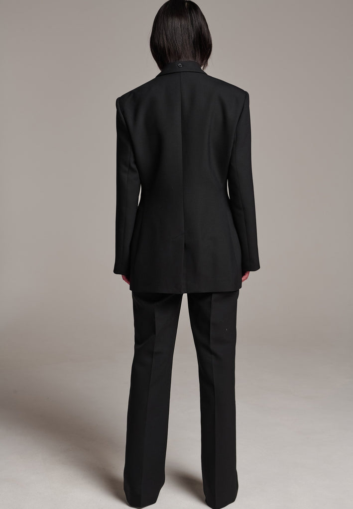 Experience flawless tailoring with this structured blazer, featuring sharp wide shoulders and a subtly cinched waist. Fully satin-lined for added luxury, it includes horn buttons and welt pockets with flaps, along with a back slit for ease of movement. Masterfully crafted in a versatile black hue, this blazer seamlessly complements a range of colors, embodying precision and elegance.