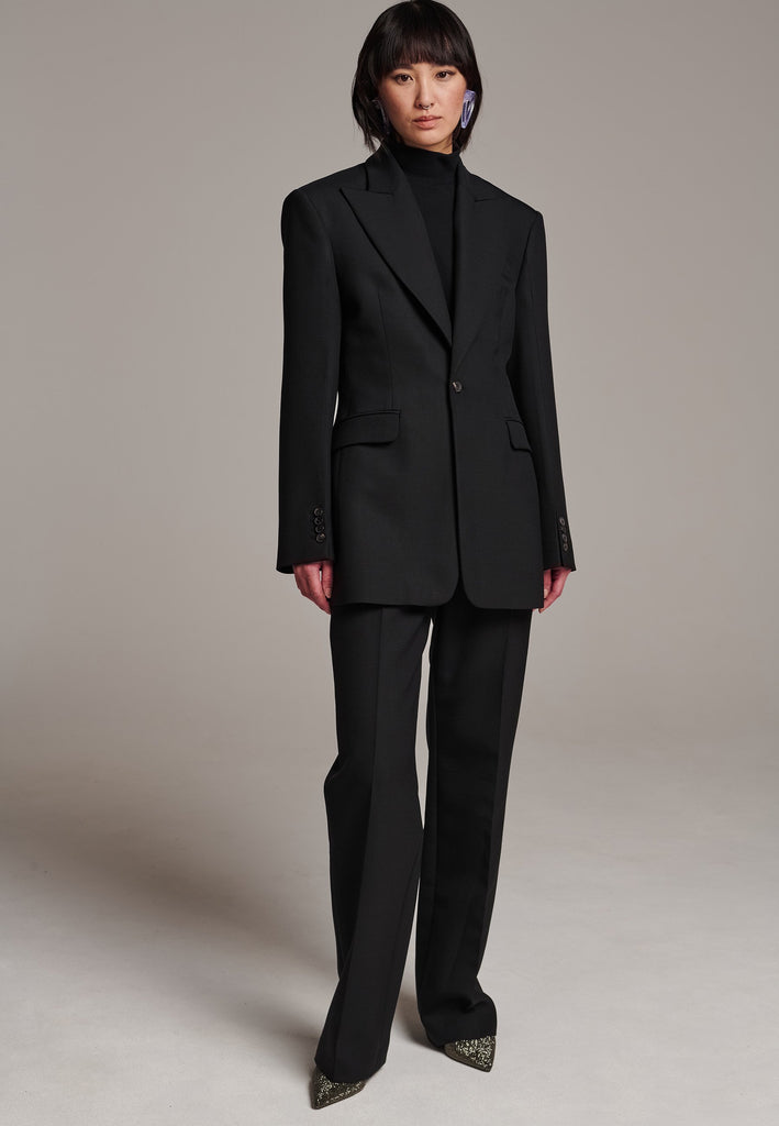 Experience flawless tailoring with this structured blazer, featuring sharp wide shoulders and a subtly cinched waist. Fully satin-lined for added luxury, it includes horn buttons and welt pockets with flaps, along with a back slit for ease of movement. Masterfully crafted in a versatile black hue, this blazer seamlessly complements a range of colors, embodying precision and elegance.