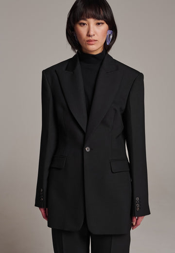Experience flawless tailoring with this structured blazer, featuring sharp wide shoulders and a subtly cinched waist. Fully satin-lined for added luxury, it includes horn buttons and welt pockets with flaps, along with a back slit for ease of movement. Masterfully crafted in a versatile black hue, this blazer seamlessly complements a range of colors, embodying precision and elegance.
