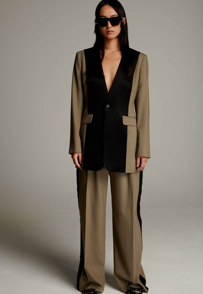 When modern minimalism meets with bold design details. Featuring a unique black panel that cuts vertically down the center front, it creates a striking contrast and edgy focal point. The no-lapel design adds a clean, streamlined aesthetic, while the tailored fit enhances its sophisticated appeal.