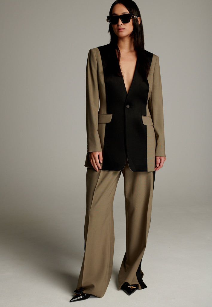 When modern minimalism meets with bold design details. Featuring a unique black panel that cuts vertically down the center front, it creates a striking contrast and edgy focal point. The no-lapel design adds a clean, streamlined aesthetic, while the tailored fit enhances its sophisticated appeal.