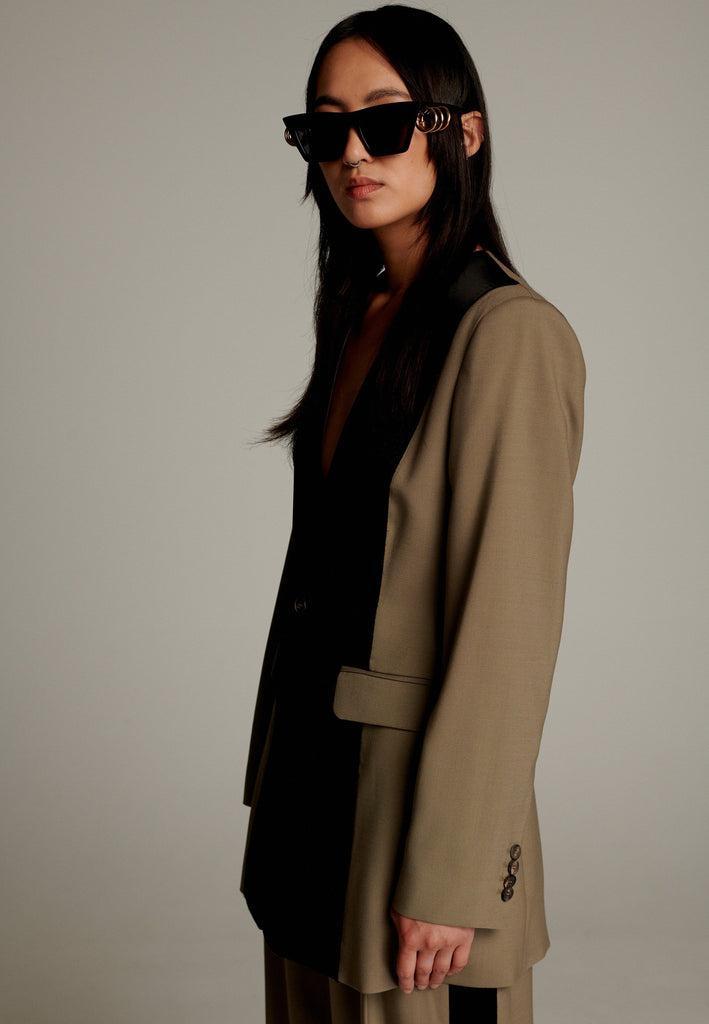 When modern minimalism meets with bold design details. Featuring a unique black panel that cuts vertically down the center front, it creates a striking contrast and edgy focal point. The no-lapel design adds a clean, streamlined aesthetic, while the tailored fit enhances its sophisticated appeal.