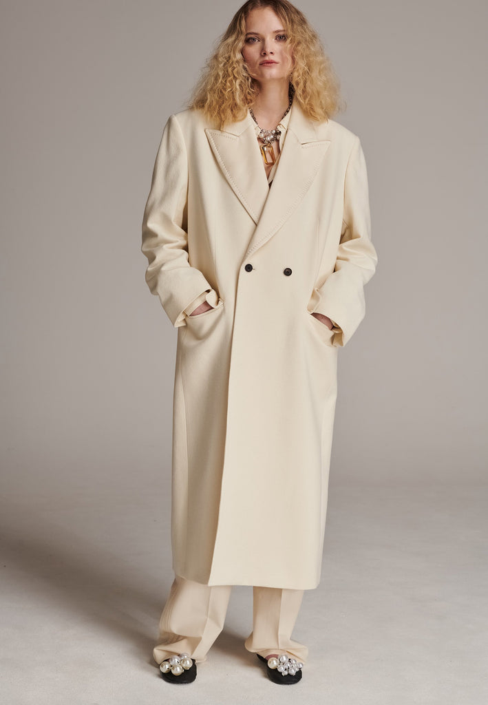 An effortless long coat to slip over any outfit. Detailed by sharp shoulder pads, double-breast fittin and square hole horn buttons. The ankle-grazing length emphasizes the loose fit and the effortless cool over tailoring. FRENKEN makes dressing up every morning easier.