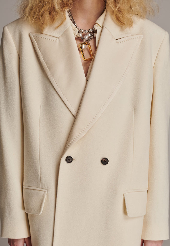 An effortless long coat to slip over any outfit. Detailed by sharp shoulder pads, double-breast fittin and square hole horn buttons. The ankle-grazing length emphasizes the loose fit and the effortless cool over tailoring. FRENKEN makes dressing up every morning easier.