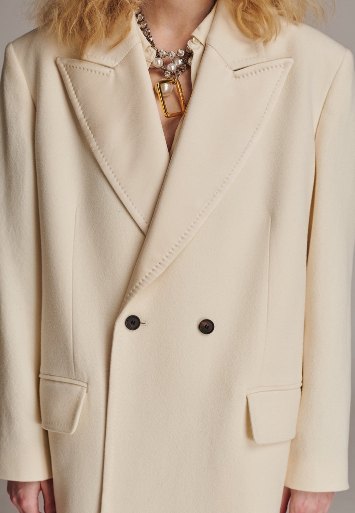 An effortless long coat to slip over any outfit. Detailed by sharp shoulder pads, double-breast fittin and square hole horn buttons. The ankle-grazing length emphasizes the loose fit and the effortless cool over tailoring. FRENKEN makes dressing up every morning easier.