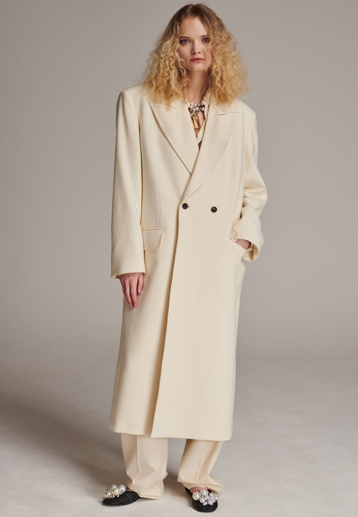 An effortless long coat to slip over any outfit. Detailed by sharp shoulder pads, double-breast fittin and square hole horn buttons. The ankle-grazing length emphasizes the loose fit and the effortless cool over tailoring. FRENKEN makes dressing up every morning easier.