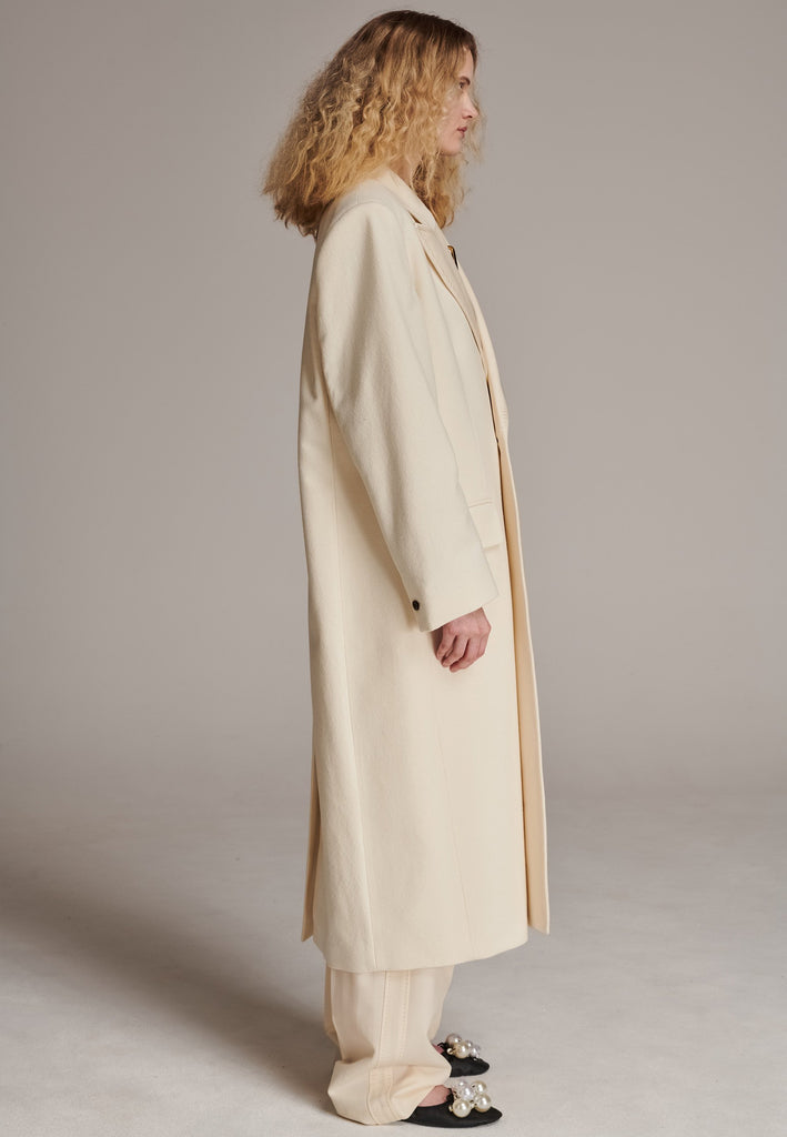 An effortless long coat to slip over any outfit. Detailed by sharp shoulder pads, double-breast fittin and square hole horn buttons. The ankle-grazing length emphasizes the loose fit and the effortless cool over tailoring. FRENKEN makes dressing up every morning easier.