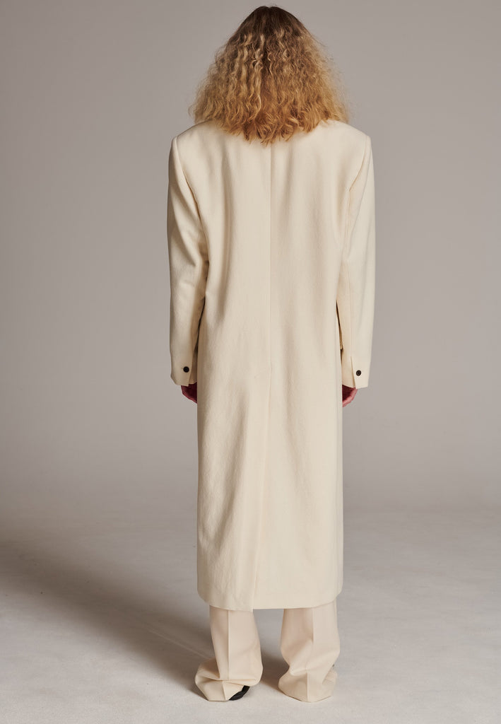 An effortless long coat to slip over any outfit. Detailed by sharp shoulder pads, double-breast fittin and square hole horn buttons. The ankle-grazing length emphasizes the loose fit and the effortless cool over tailoring. FRENKEN makes dressing up every morning easier.
