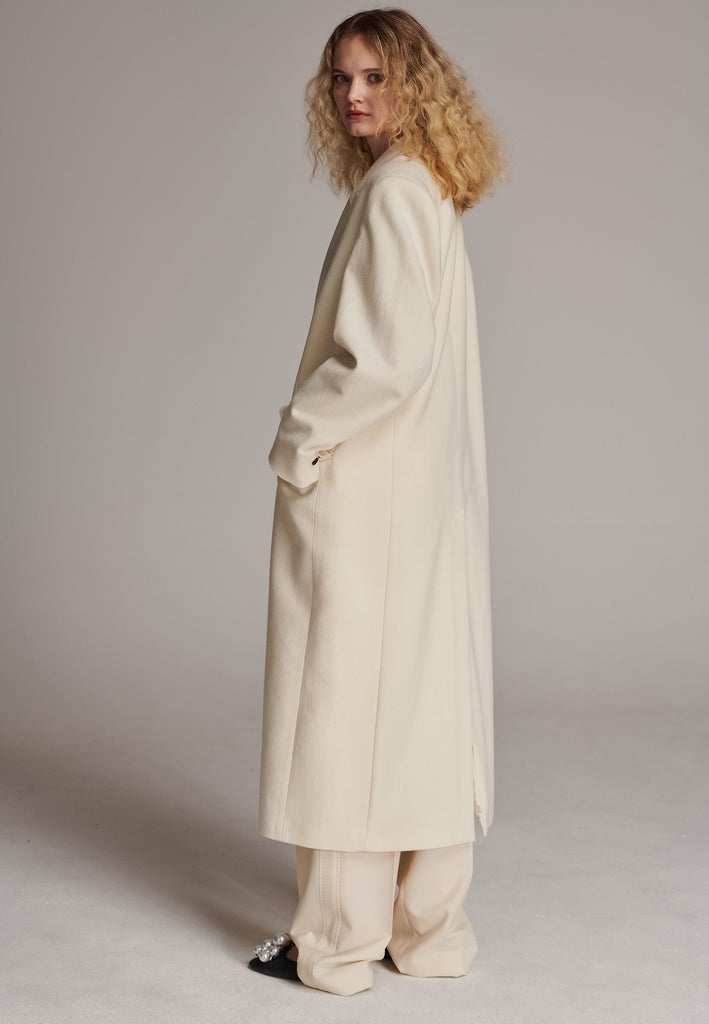 An effortless long coat to slip over any outfit. Detailed by sharp shoulder pads, double-breast fittin and square hole horn buttons. The ankle-grazing length emphasizes the loose fit and the effortless cool over tailoring. FRENKEN makes dressing up every morning easier.