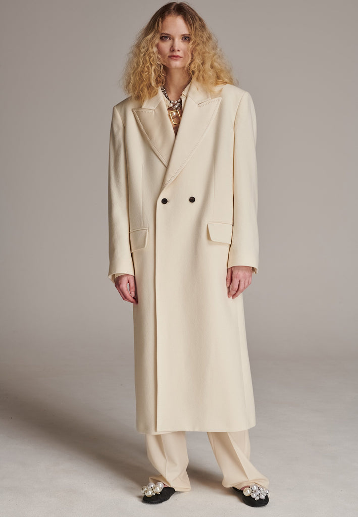 An effortless long coat to slip over any outfit. Detailed by sharp shoulder pads, double-breast fittin and square hole horn buttons. The ankle-grazing length emphasizes the loose fit and the effortless cool over tailoring. FRENKEN makes dressing up every morning easier.