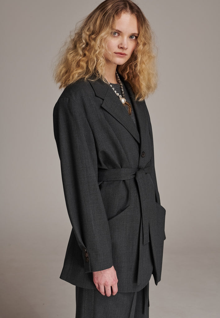 Oversized wrap blazer cut from a wool blend. Designed for an oversized fit, cut to be worn very loose. Padded wide round shoulders that add structure to the loose fit. Knot the inserted belt at the back or front to customize the shape. Horn button closure, welt pocket at front. Central vent at back hem. Full viscose satin lining and detailed with a needlepoint on the belt. This longline silhouette is perfectly tailored and could be your everyday rotation blazer.