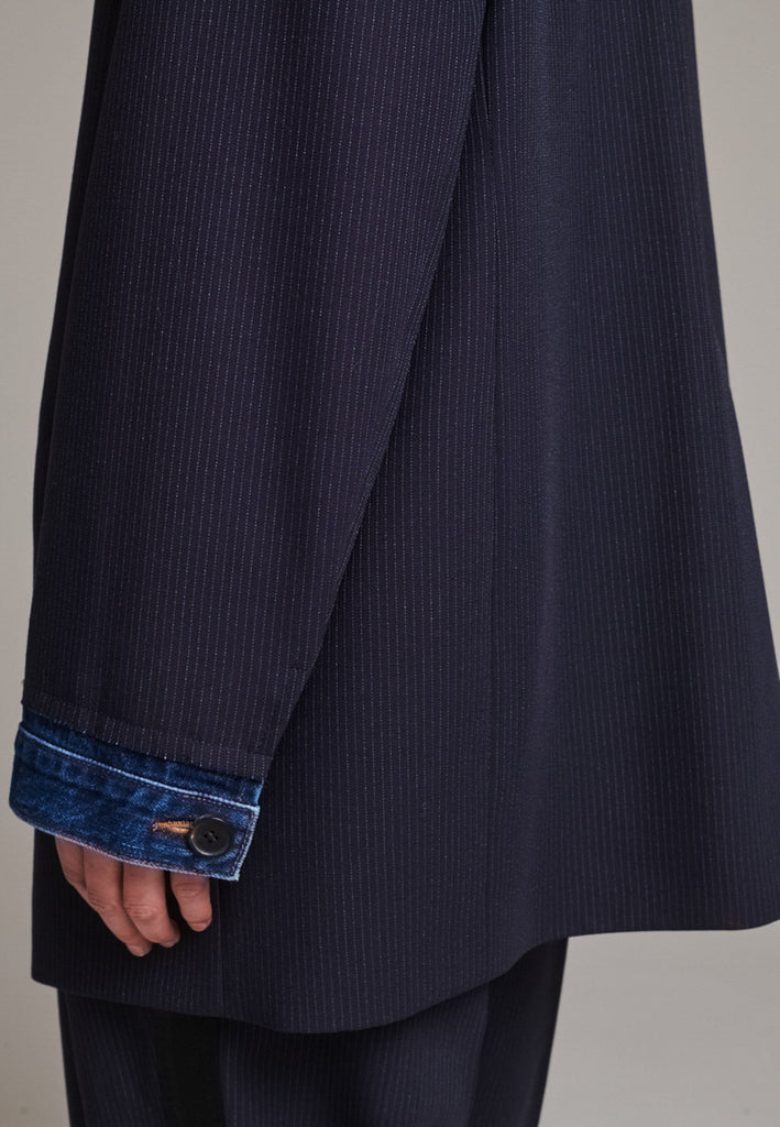The Devotion Pinstripe Blazer Navy is a bold, reimagined take on classic tailoring. Designed with an oversized silhouette, it features a timeless navy pinstripe base contrasted by sleek black lapels in a subtly glossy fabric, adding a refined, modern twist. The cuffs break convention with a denim finish, introducing a casual edge to the otherwise structured piece. 
