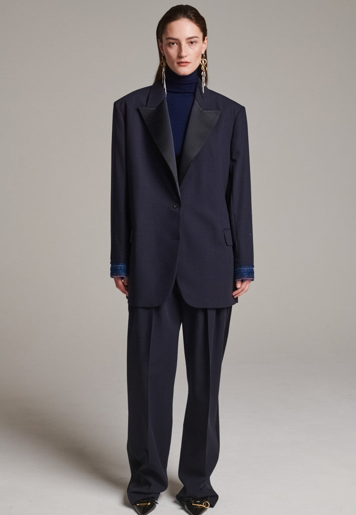 The Devotion Pinstripe Blazer Navy is a bold, reimagined take on classic tailoring. Designed with an oversized silhouette, it features a timeless navy pinstripe base contrasted by sleek black lapels in a subtly glossy fabric, adding a refined, modern twist. The cuffs break convention with a denim finish, introducing a casual edge to the otherwise structured piece. 