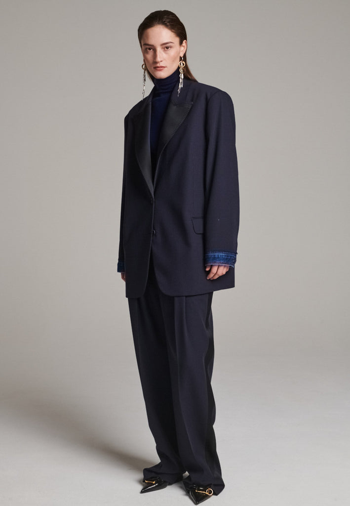 The Devotion Pinstripe Blazer Navy is a bold, reimagined take on classic tailoring. Designed with an oversized silhouette, it features a timeless navy pinstripe base contrasted by sleek black lapels in a subtly glossy fabric, adding a refined, modern twist. The cuffs break convention with a denim finish, introducing a casual edge to the otherwise structured piece. 