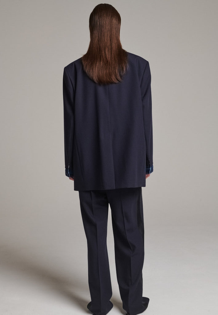 The Devotion Pinstripe Blazer Navy is a bold, reimagined take on classic tailoring. Designed with an oversized silhouette, it features a timeless navy pinstripe base contrasted by sleek black lapels in a subtly glossy fabric, adding a refined, modern twist. The cuffs break convention with a denim finish, introducing a casual edge to the otherwise structured piece. 