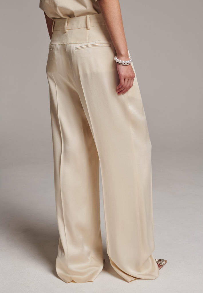 These deconstructed trousers combine a tailored wool top with a raw-edge finish, seamlessly attached to wide crepe satin legs that fall elegantly. The flat pleats create a slimmimg effect at the waist, enhancing the voluminous look of the wide legs. The pressed seam elongated the legs, ensuring a striking and sophisticated silhouette.