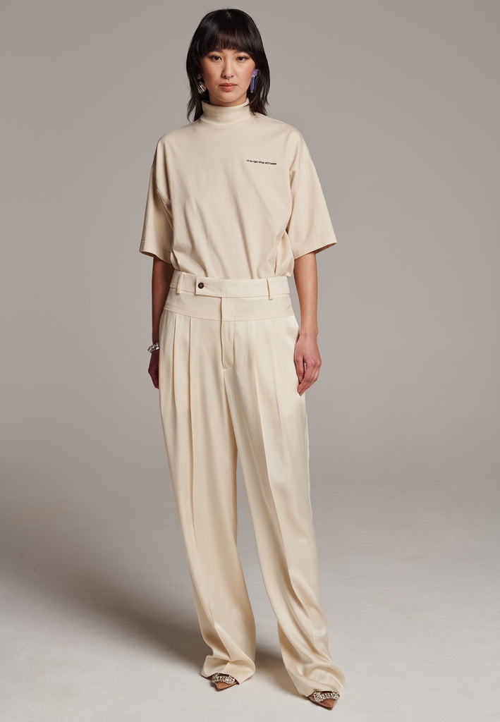 These deconstructed trousers combine a tailored wool top with a raw-edge finish, seamlessly attached to wide crepe satin legs that fall elegantly. The flat pleats create a slimmimg effect at the waist, enhancing the voluminous look of the wide legs. The pressed seam elongated the legs, ensuring a striking and sophisticated silhouette.