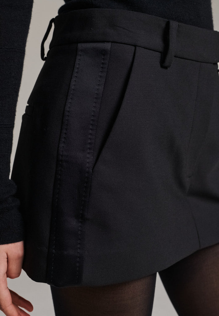 Tailored mini skirt with clean lines and a sharp silhouette. Cut from structured wool-blend suiting fabric, detailed with satin side stripes for a subtle tuxedo touch. High-rise waist with belt loops and side pockets, minimalist yet refined.