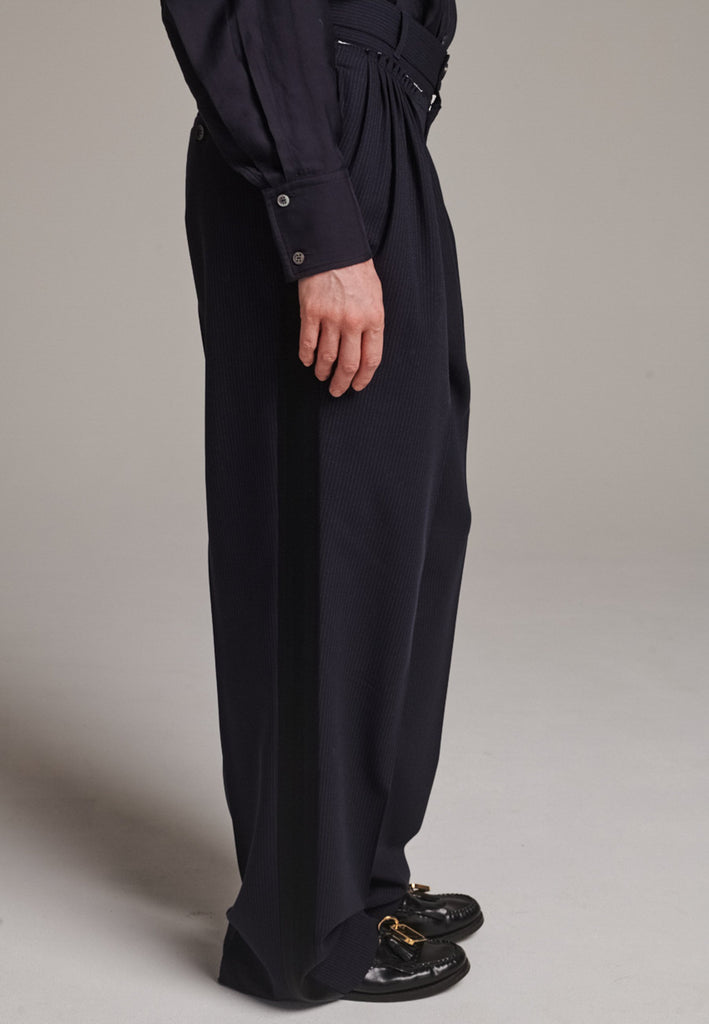 Straight-leg trousers with a classic cut, elevated by subtle yet striking details. The unfinished waistband adds a raw, intentional edge, contrasting with the otherwise clean silhouette. Glossy black fabric stripe runs down the side seams, bringing a touch of texture and definition to the navy pinstripe base. A refined everyday piece with a modern, deconstructed twist.