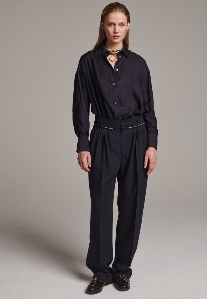 Straight-leg trousers with a classic cut, elevated by subtle yet striking details. The unfinished waistband adds a raw, intentional edge, contrasting with the otherwise clean silhouette. Glossy black fabric stripe runs down the side seams, bringing a touch of texture and definition to the navy pinstripe base. A refined everyday piece with a modern, deconstructed twist.