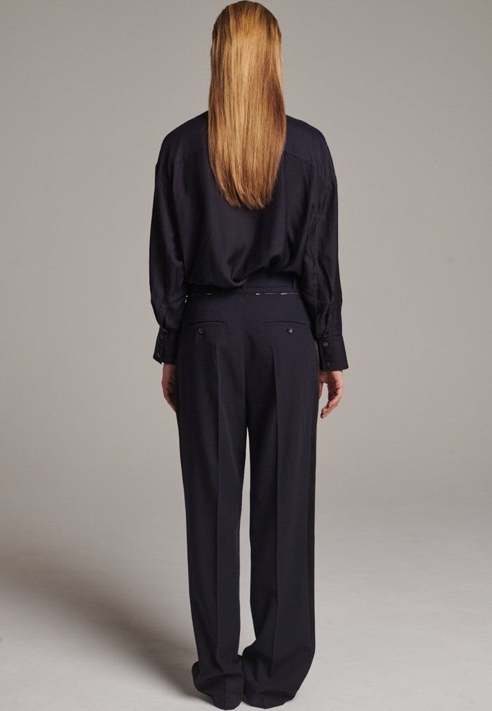 Straight-leg trousers with a classic cut, elevated by subtle yet striking details. The unfinished waistband adds a raw, intentional edge, contrasting with the otherwise clean silhouette. Glossy black fabric stripe runs down the side seams, bringing a touch of texture and definition to the navy pinstripe base. A refined everyday piece with a modern, deconstructed twist.