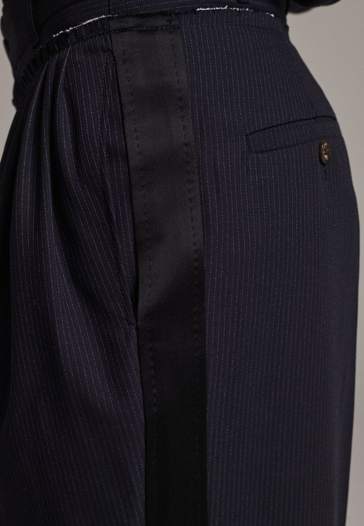 Straight-leg trousers with a classic cut, elevated by subtle yet striking details. The unfinished waistband adds a raw, intentional edge, contrasting with the otherwise clean silhouette. Glossy black fabric stripe runs down the side seams, bringing a touch of texture and definition to the navy pinstripe base. A refined everyday piece with a modern, deconstructed twist.