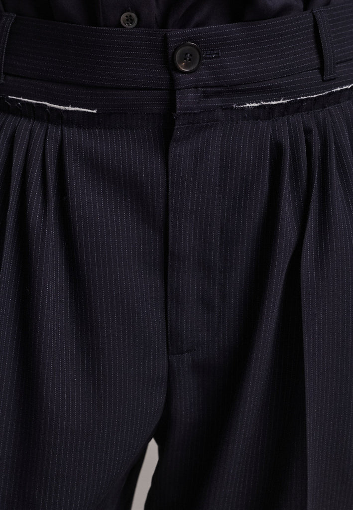Straight-leg trousers with a classic cut, elevated by subtle yet striking details. The unfinished waistband adds a raw, intentional edge, contrasting with the otherwise clean silhouette. Glossy black fabric stripe runs down the side seams, bringing a touch of texture and definition to the navy pinstripe base. A refined everyday piece with a modern, deconstructed twist.