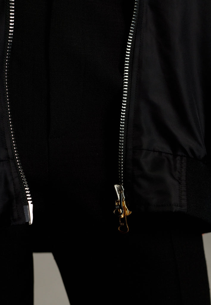 A bomber jacket combines modern utility with sleek style, this one features a unique silver and gold zipper detail, adding a touch of metallic contrast to its minimalist design. The bomber silhouette offers a relaxed, casual vibe, while its durable nylon fabric ensures both comfort and functionality. This versatile jacket effortlessly blends style and practicality, making it a timeless addition to any wardrobe.