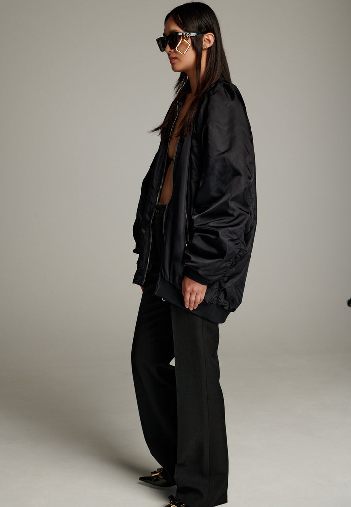 A bomber jacket combines modern utility with sleek style, this one features a unique silver and gold zipper detail, adding a touch of metallic contrast to its minimalist design. The bomber silhouette offers a relaxed, casual vibe, while its durable nylon fabric ensures both comfort and functionality. This versatile jacket effortlessly blends style and practicality, making it a timeless addition to any wardrobe.