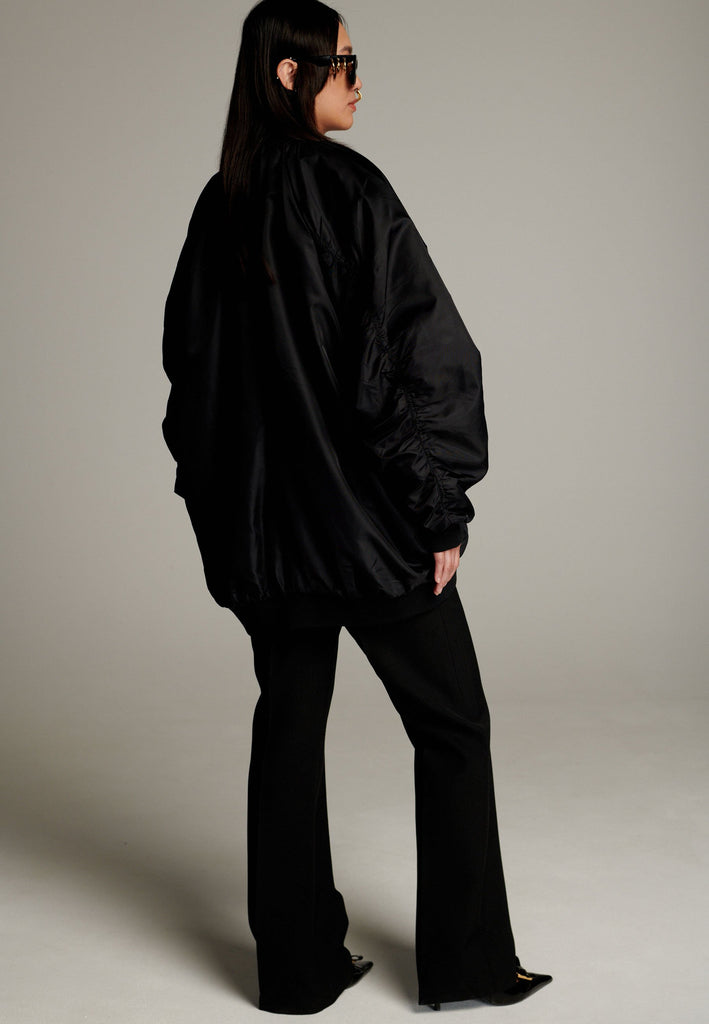 A bomber jacket combines modern utility with sleek style, this one features a unique silver and gold zipper detail, adding a touch of metallic contrast to its minimalist design. The bomber silhouette offers a relaxed, casual vibe, while its durable nylon fabric ensures both comfort and functionality. This versatile jacket effortlessly blends style and practicality, making it a timeless addition to any wardrobe.