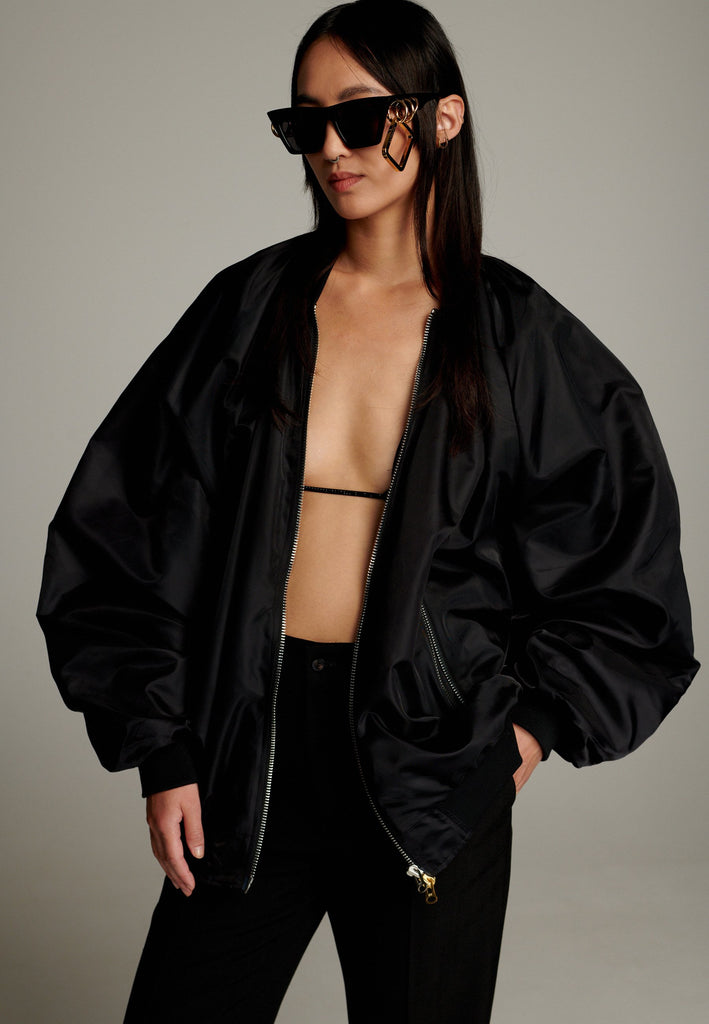 A bomber jacket combines modern utility with sleek style, this one features a unique silver and gold zipper detail, adding a touch of metallic contrast to its minimalist design. The bomber silhouette offers a relaxed, casual vibe, while its durable nylon fabric ensures both comfort and functionality. This versatile jacket effortlessly blends style and practicality, making it a timeless addition to any wardrobe.