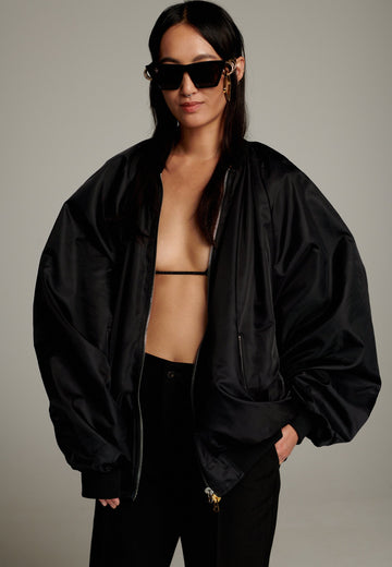 A bomber jacket combines modern utility with sleek style, this one features a unique silver and gold zipper detail, adding a touch of metallic contrast to its minimalist design. The bomber silhouette offers a relaxed, casual vibe, while its durable nylon fabric ensures both comfort and functionality. This versatile jacket effortlessly blends style and practicality, making it a timeless addition to any wardrobe.