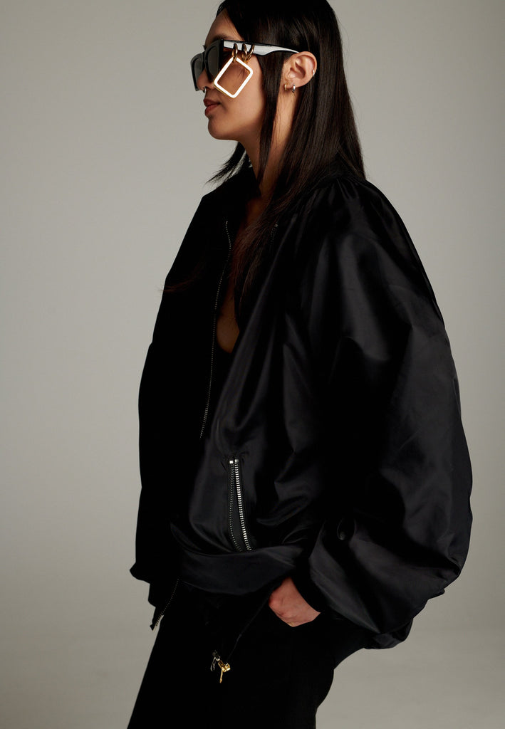 A bomber jacket combines modern utility with sleek style, this one features a unique silver and gold zipper detail, adding a touch of metallic contrast to its minimalist design. The bomber silhouette offers a relaxed, casual vibe, while its durable nylon fabric ensures both comfort and functionality. This versatile jacket effortlessly blends style and practicality, making it a timeless addition to any wardrobe.