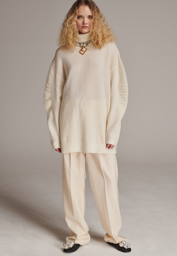Stay warm and stylish with this oversized knitted sweater, crafted from luxurious virgin merino wool that gives a soft handle. Dropped shoulder seam detailed with gathering at the sleeves, it combines a cozy turtleneck with designer flair. The off-white shade works especially well with off-white tailoring and jeans. Designed for an oversized fit, cut to be worn very loose. Long in sleeves. This piece ensures you’ll stay snug and chic, even on the coldest days.