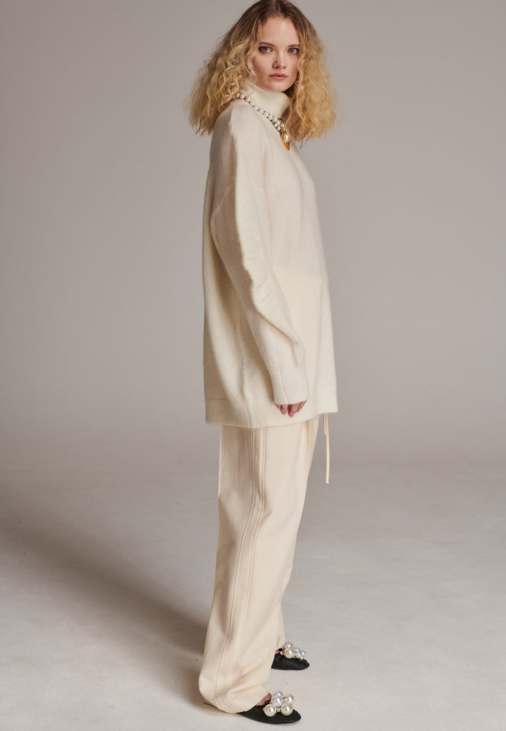 Stay warm and stylish with this oversized knitted sweater, crafted from luxurious virgin merino wool that gives a soft handle. Dropped shoulder seam detailed with gathering at the sleeves, it combines a cozy turtleneck with designer flair. The off-white shade works especially well with off-white tailoring and jeans. Designed for an oversized fit, cut to be worn very loose. Long in sleeves. This piece ensures you’ll stay snug and chic, even on the coldest days.