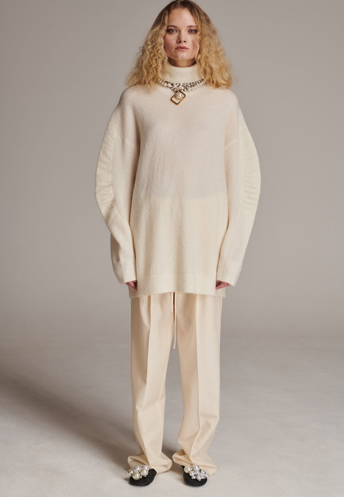 Stay warm and stylish with this oversized knitted sweater, crafted from luxurious virgin merino wool that gives a soft handle. Dropped shoulder seam detailed with gathering at the sleeves, it combines a cozy turtleneck with designer flair. The off-white shade works especially well with off-white tailoring and jeans. Designed for an oversized fit, cut to be worn very loose. Long in sleeves. This piece ensures you’ll stay snug and chic, even on the coldest days.