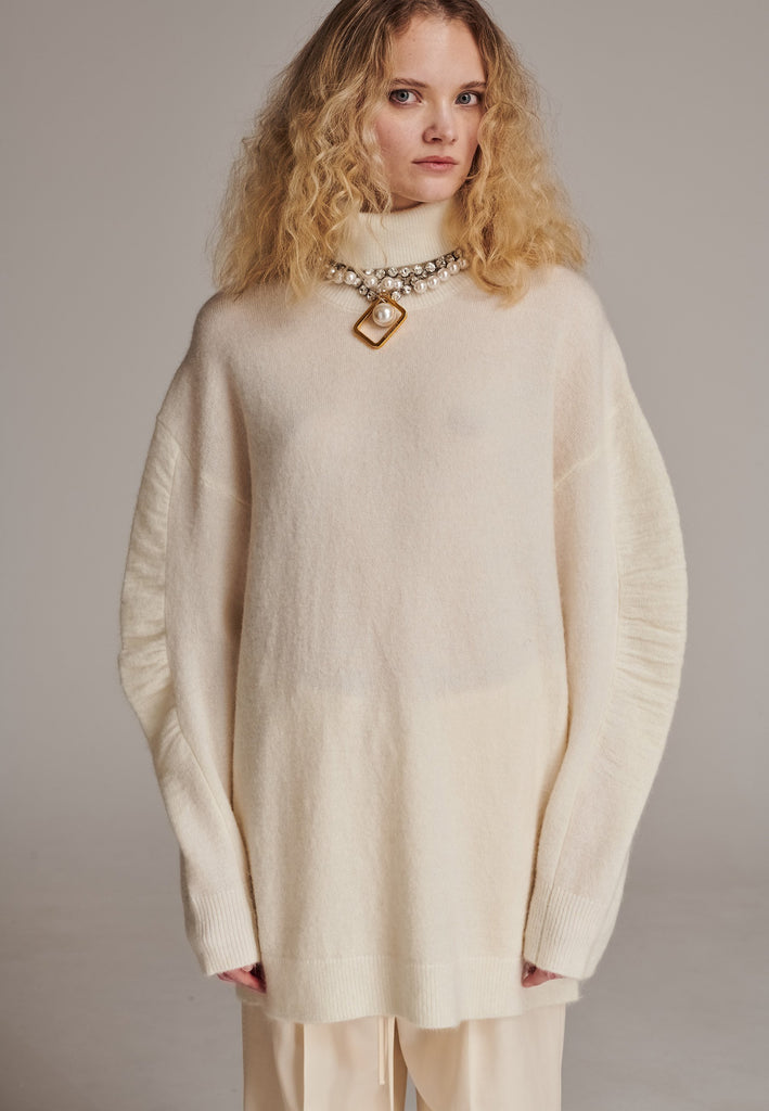 Stay warm and stylish with this oversized knitted sweater, crafted from luxurious virgin merino wool that gives a soft handle. Dropped shoulder seam detailed with gathering at the sleeves, it combines a cozy turtleneck with designer flair. The off-white shade works especially well with off-white tailoring and jeans. Designed for an oversized fit, cut to be worn very loose. Long in sleeves. This piece ensures you’ll stay snug and chic, even on the coldest days.